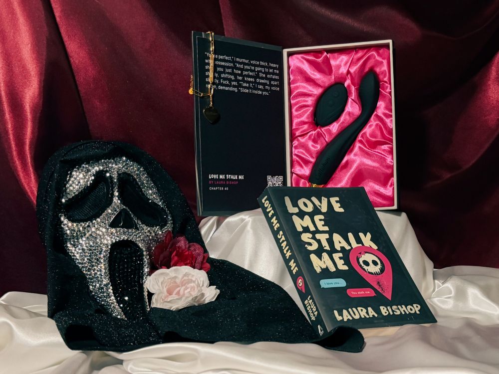 The Callahan silicone toy vibrator in the opened book-like package for Love Me Stalk Me by Laura Bishop and the gold bracelet next to a ghostface mask and the book Love Me Stalk Me.