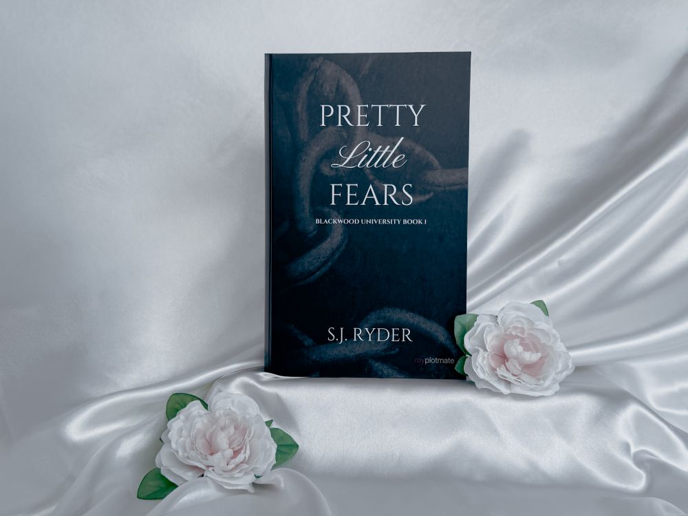 The front cover of the book-like package for Pretty Little Fears by S.J. Ryder next to two white roses.