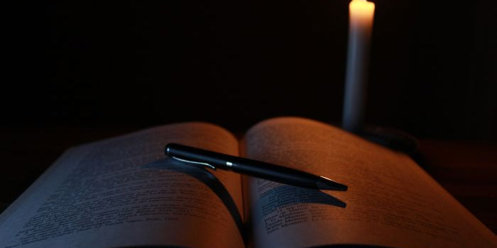 An opened book with a pen on it next to a candle.