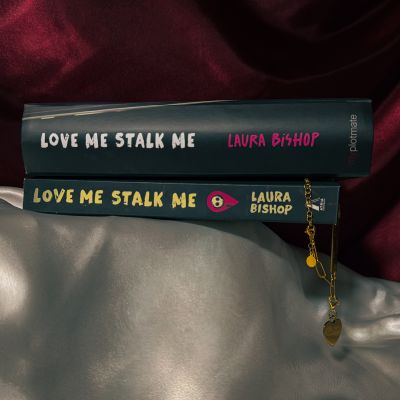The closed box for the dark romance book Love Me Stalk Me next to the actual book of Laura Bishop presenting the custom gold charm with the name Callahan engraved.