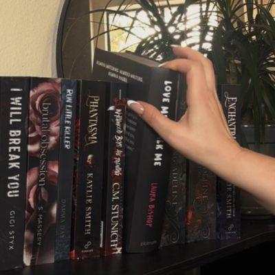 The closed box for the dark romance book Love Me Stalk Me being pulled from the bookshelf by a female hand.