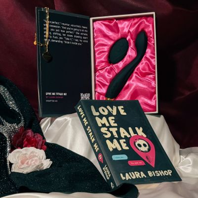 The opened box for the dark romance book Love Me Stalk Me presenting the toy Callahan and the custom gold charm with Callahan engraved, next to the actual book from Laura Bishop.