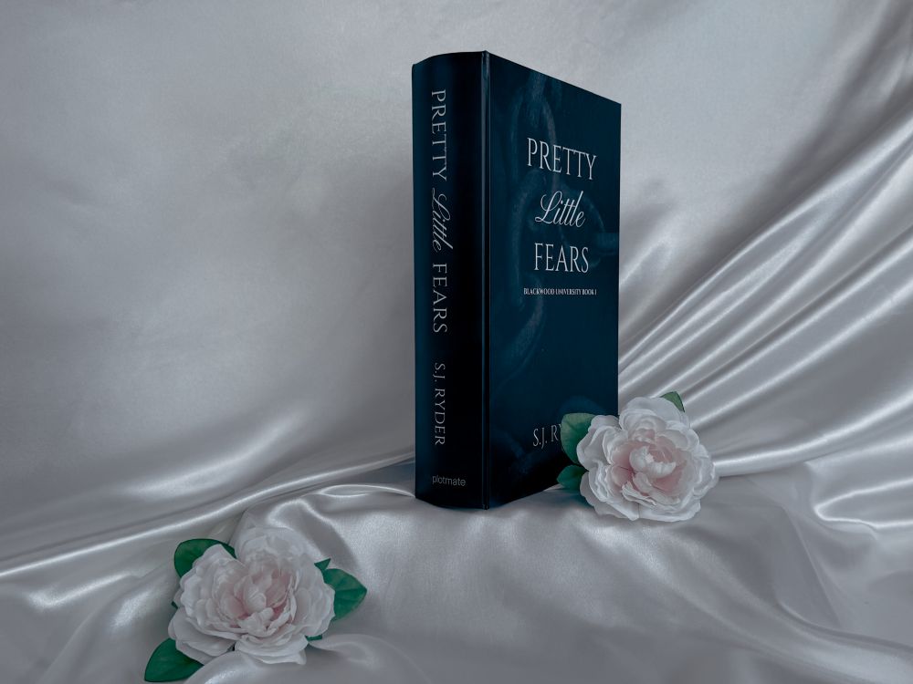 The front cover and spine of the book-like package for Pretty Little Fears by S.J. Ryder next to two white roses.