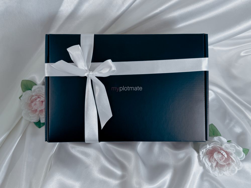 The myplotmate box with a white ribbon and two roses next to it.