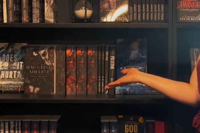 A woman pointing to a bookshelf with dark romance books. 