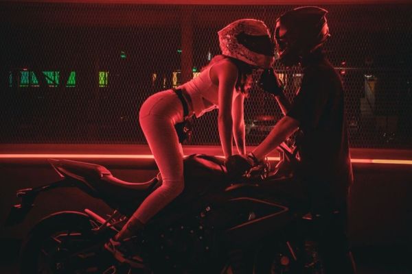 A biker girl leaning across her bike towards a male biker.