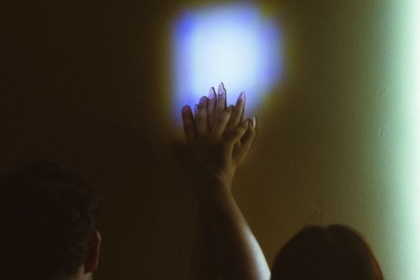 The hand of a woman and a man together pushed against a wall.