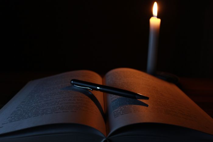 An opened book with a pen on it next to a candle.